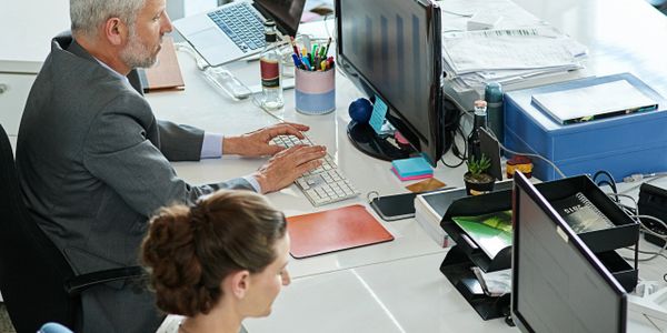 Two professionals working at their desks with computers and documents.