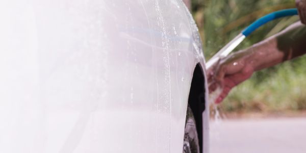 Person washing a white car with a blue hose outdoors.
