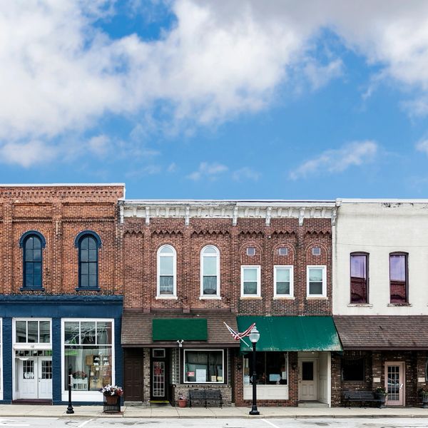 Historic brick storefronts line a small town street under a blue sky.
