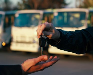 Handing over a car key in front of parked vehicles.