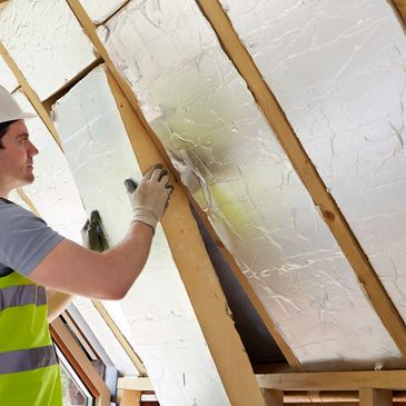 Worker installing foil insulation in attic under construction.