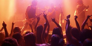 Rock band performing live with enthusiastic crowd raising their hands.