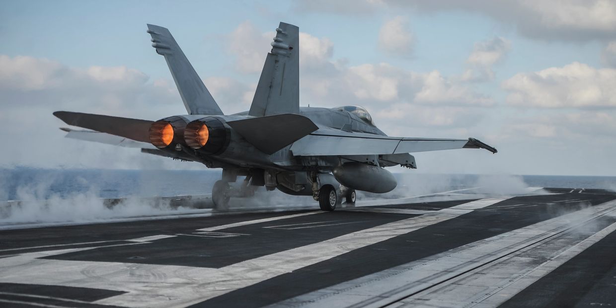 A fighter jet taking off from an aircraft carrier with afterburners on.