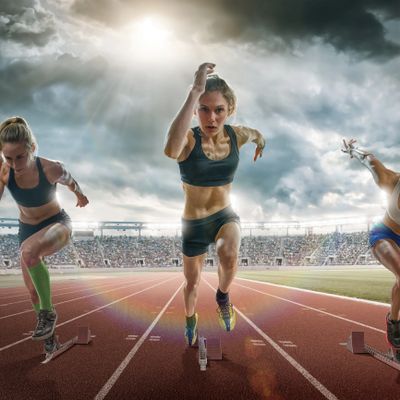 Three female athletes sprinting on a track during a race under dramatic skies.