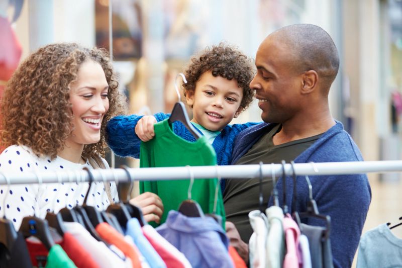 Family Looking At Clothes On Rail In Shopping Mall Having Fun