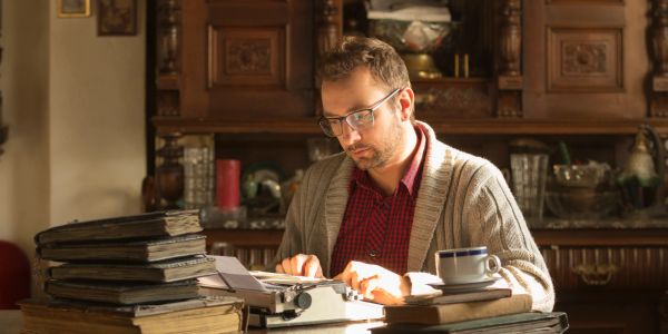 Man typing on a typewriter at a cluttered desk.