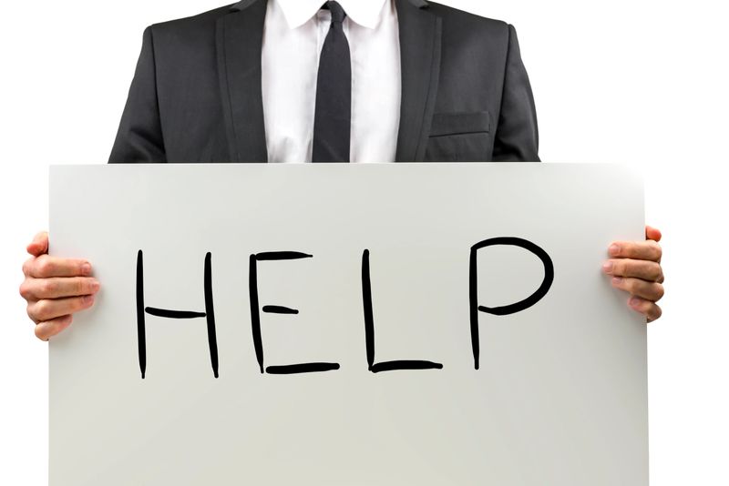 Businessman holding a white sign with the handwritten word - Help - in front of him, close up torso view isolated on white.