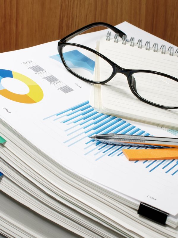 Stack of business reports with glasses, notepad, pen, and sticky notes on top.