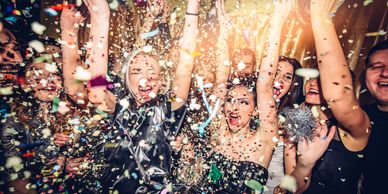 A lively group of people celebrating with confetti and raised hands.