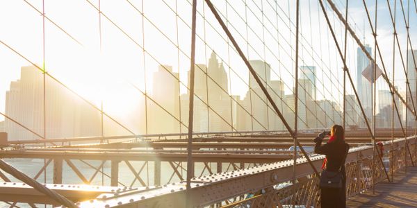 Person photographing city skyline from a sunlit bridge.