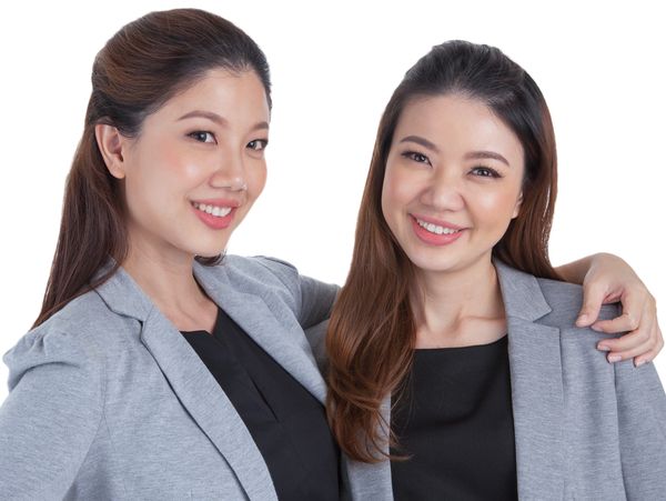 Two smiling women in gray blazers posing together against a white background.