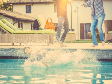 Kids jumping into a pool on a sunny day.