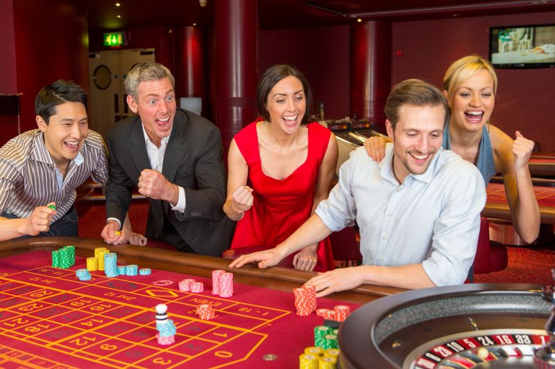 A group of happy friends play on a roulette table in a casino.
