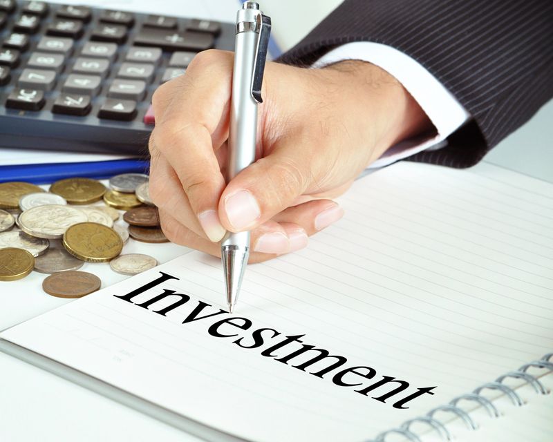 Hand with pen pointing to Investment word on the paper - financial & business concept
