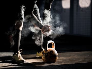 Athlete claps chalked hands near a kettlebell in a dim gym.