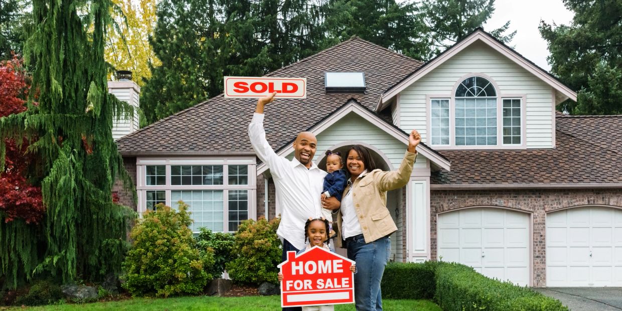 Happy family celebrates buying a new home with sold signs.