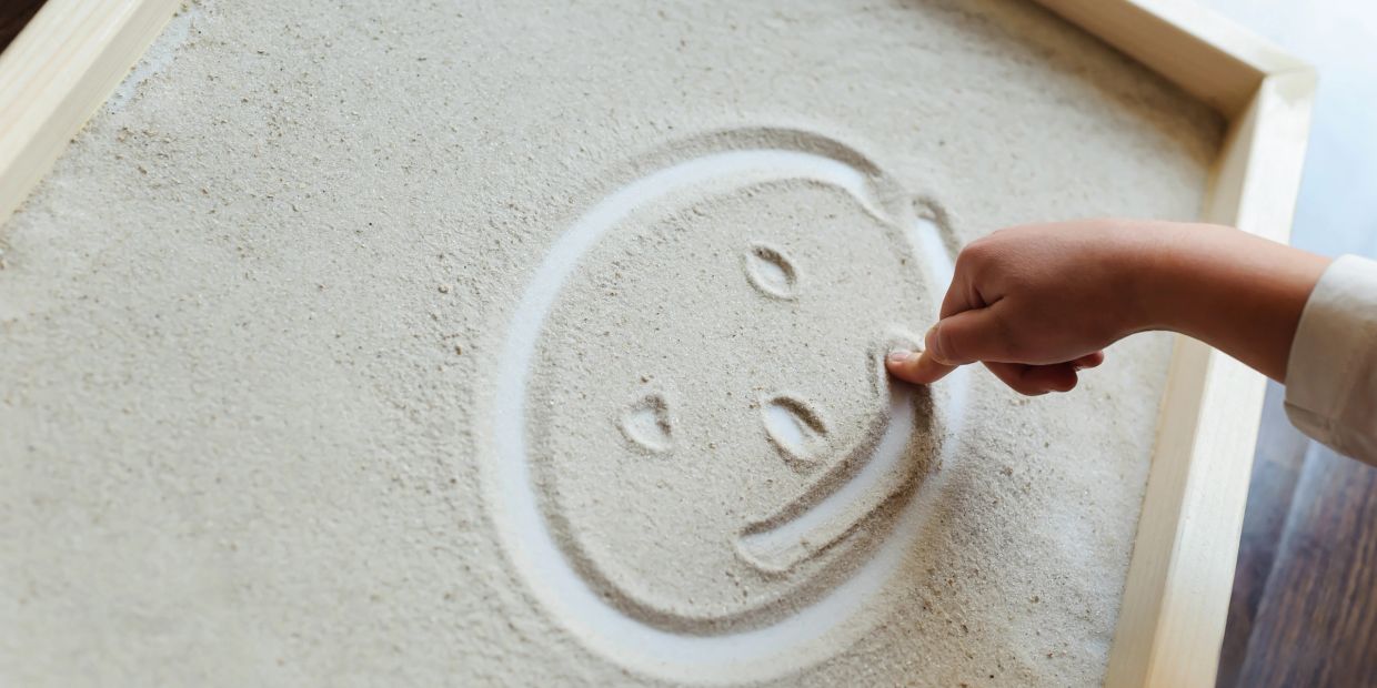 Finger drawing a smiley face in sand.