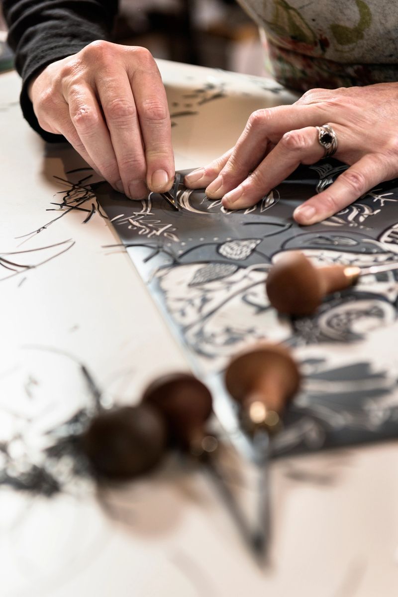 Close up portrait of a printmakers hands at work as she cuts away at the surface of a piece of lino to reveal a pattern. She is working on preparing a linocut by marking out a pattern then cutting the lino with a range of hand held cutting tools. Vertical format with a shallow focus on the artists hands giving a nice out of focus foreground. Photographed at a her artists studio on the island of Møn Denmark.
