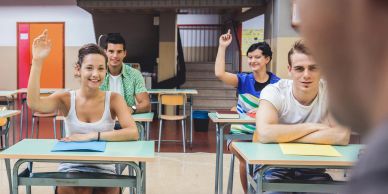 Students in a classroom eagerly raise their hands to answer.