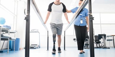 Man with a prosthetic leg walking with assistance in a rehabilitation center.