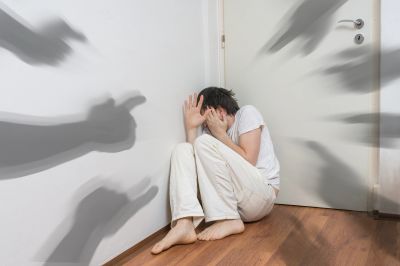 Person scared in corner from shadowy hands.