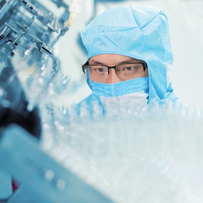 Scientist in protective gear inspecting lab equipment carefully.