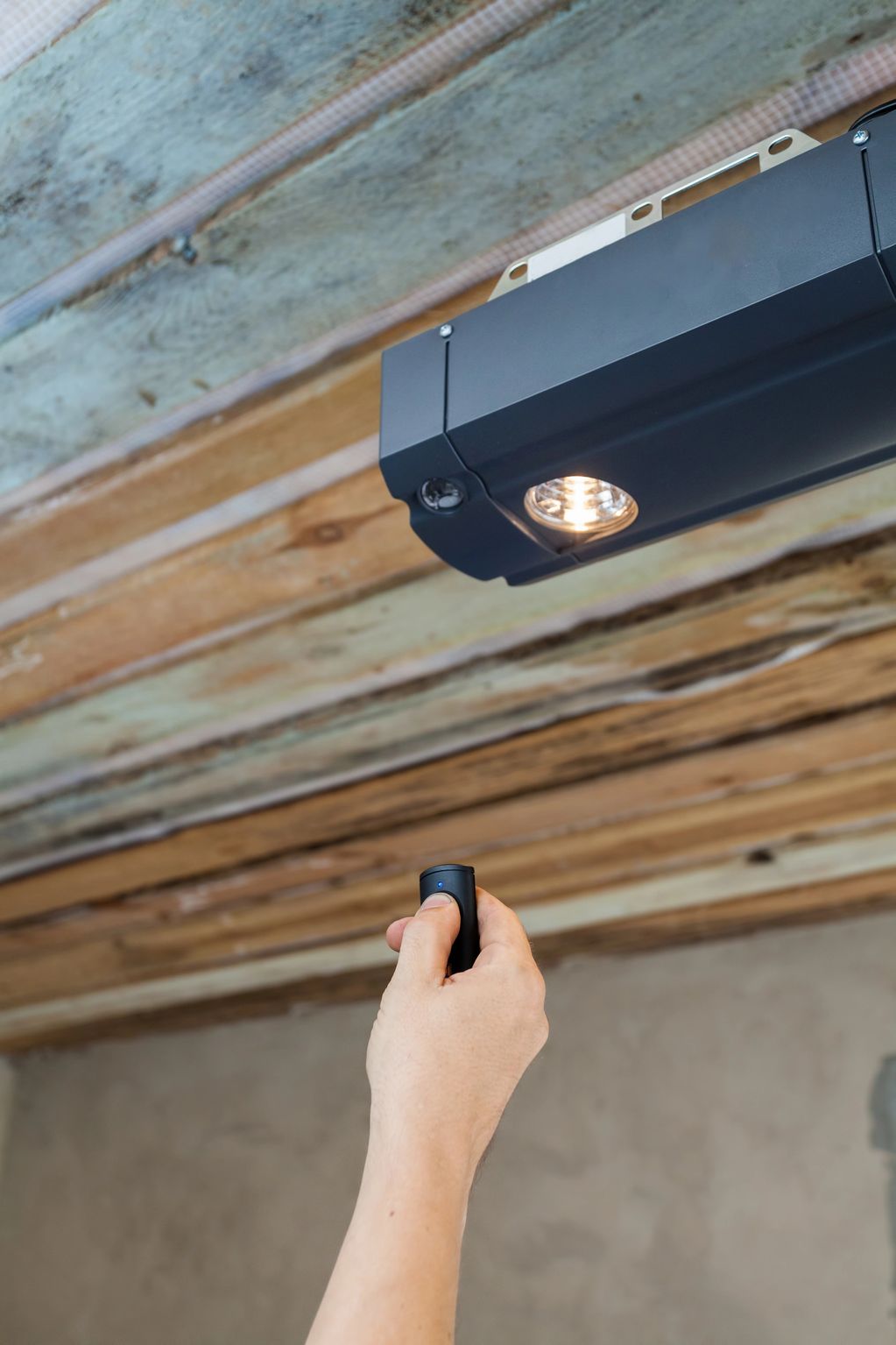 Hand holding a remote control, pointing at a ceiling light fixture.