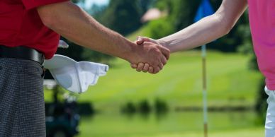 Two people shaking hands on a golf course.
