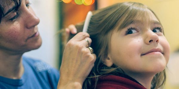 A woman combs a young girl's hair gently indoors.