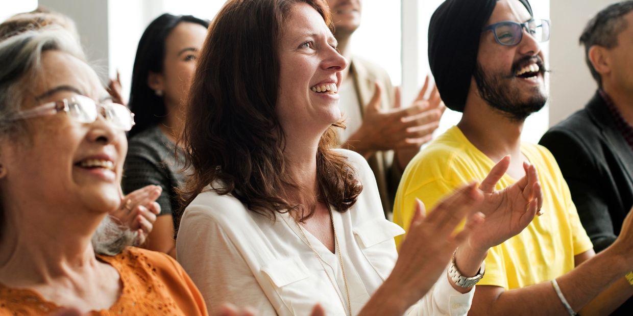 A diverse group of people clapping and smiling in a bright room.