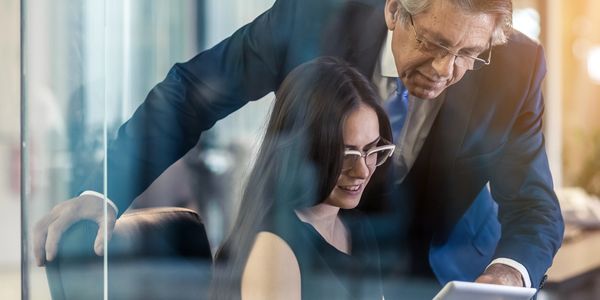Older man mentoring younger woman in a professional office setting.