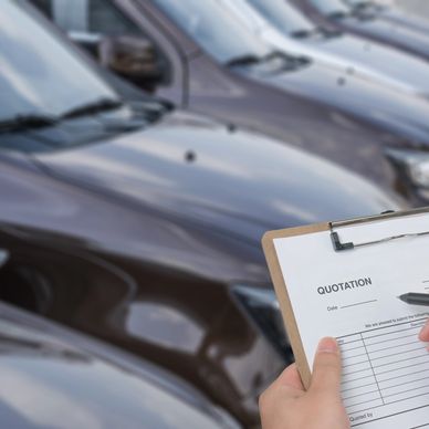 Person holding a quotation clipboard near parked cars.