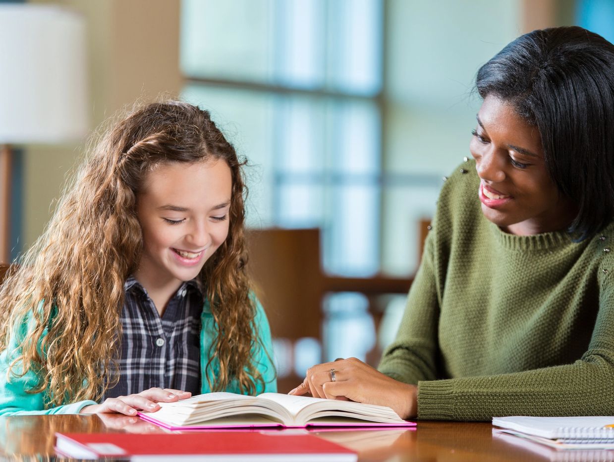 Woman tutoring a girl with a book.