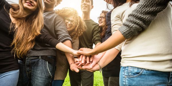 A group of friends stacking hands in a show of unity outdoors.