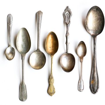 A collection of seven vintage spoons of various sizes and designs on a white background.