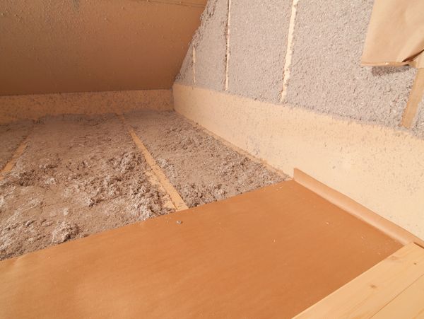 Close-up of attic insulation with blown in cellulose material and wooden beams.