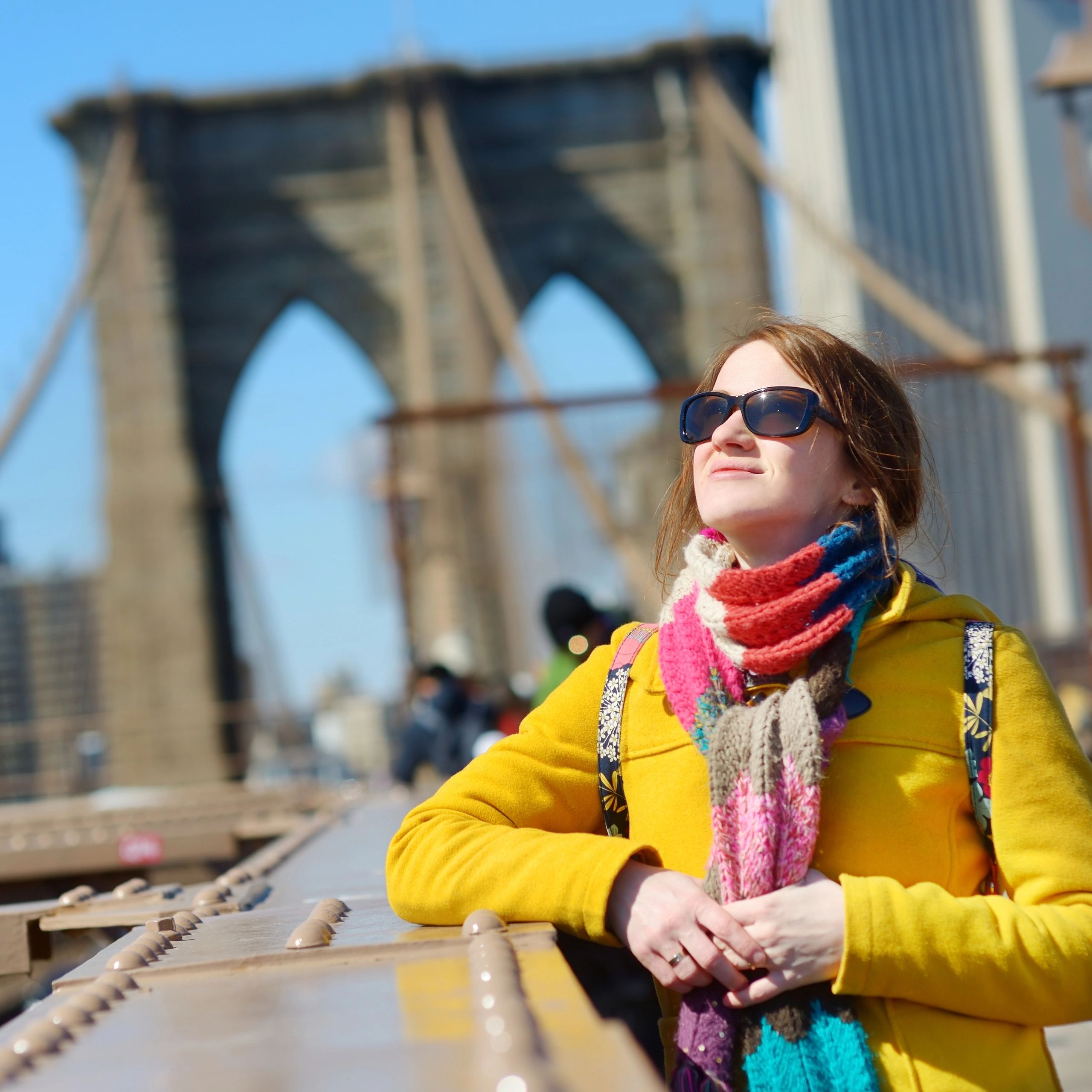 Woman in colorful scarf and yellow coat on Brooklyn Bridge.
