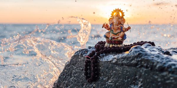 Small statue of Lord Ganesha on a rock by the ocean at sunset.