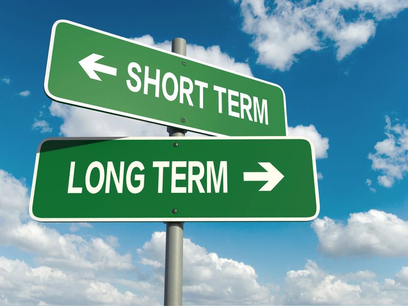A road sign with short term long term words on sky background