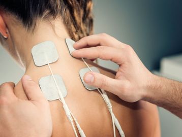 A young woman looks away from the camera as four square patches attached to wires stick on her back.