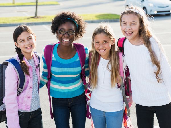 Four smiling schoolgirls with backpacks standing outdoors.