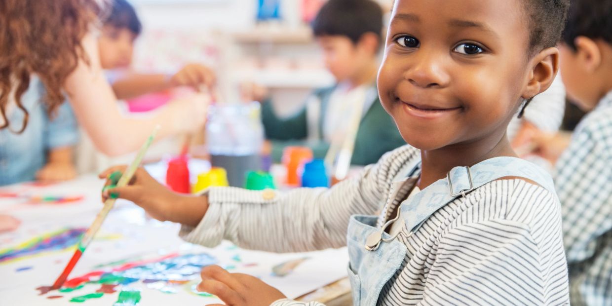 A young child smiling while painting with others at a table.