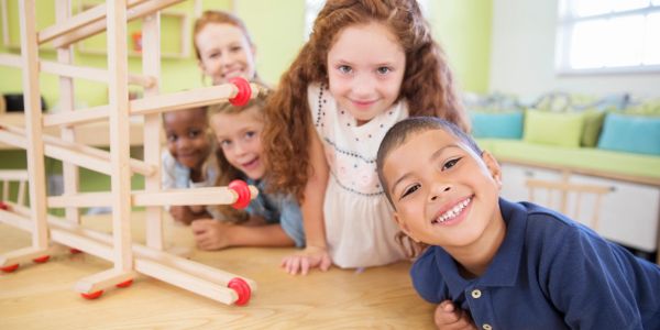 A group of smiling children leaning on a table with an overturned chair.