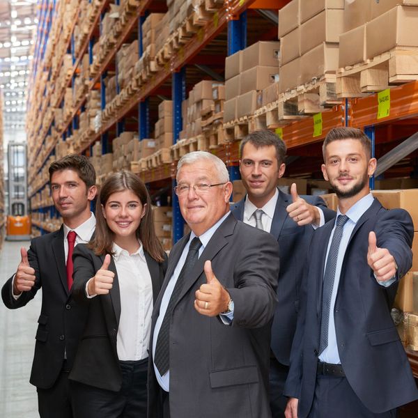 Business team in a warehouse giving thumbs up, showing success and confidence.