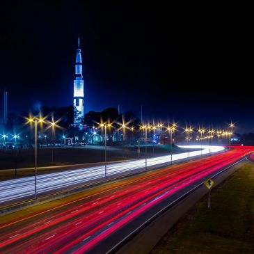 Long exposure of highway lights at night with a tall tower.