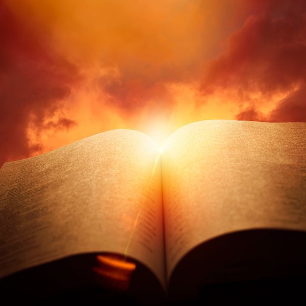 Open book glowing with sunlight against a dramatic sky.