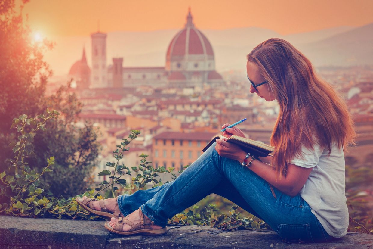 Woman writing in a notebook with a sunset view of Florence in the background.