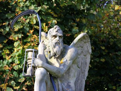 Stone statue of an angel holding an hourglass and a scythe.