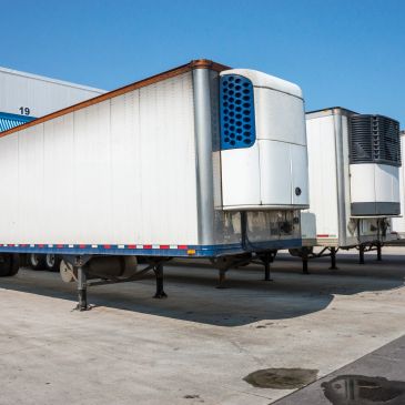 Two refrigerated semi-trailers parked outside a warehouse.