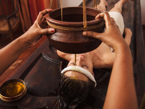 Woman receiving traditional Ayurvedic oil treatment on forehead.